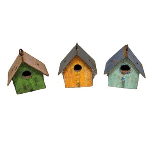 May include: Three small birdhouses with weathered, distressed finishes. One is green with a brown roof, one is yellow with a dark gray roof, and one is light blue with a dark gray roof. Each features a circular entrance hole and a metal hanging loop.