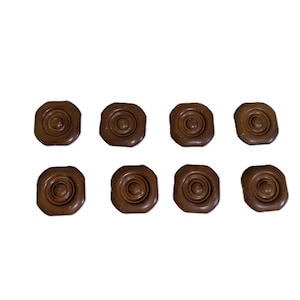 May include: Eight brown buttons arranged in two rows of four. Each button features a square shape with rounded corners and a raised, circular, concentric ring pattern centered on the surface, creating a textured, layered appearance.