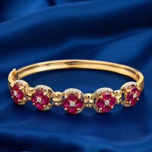 May include: A gold hinged bangle bracelet featuring five circular floral motifs. Each motif contains four oval-cut deep red rubies arranged in a clover pattern, accented with small white diamonds at the center and along the circular borders.