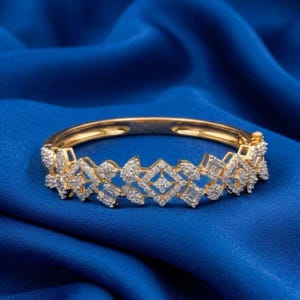 May include: A gold bracelet with a diamond design. The bracelet has a series of geometric shapes and is set against a blue background. The diamonds are clear and sparkle, adding to the bracelet's elegance.