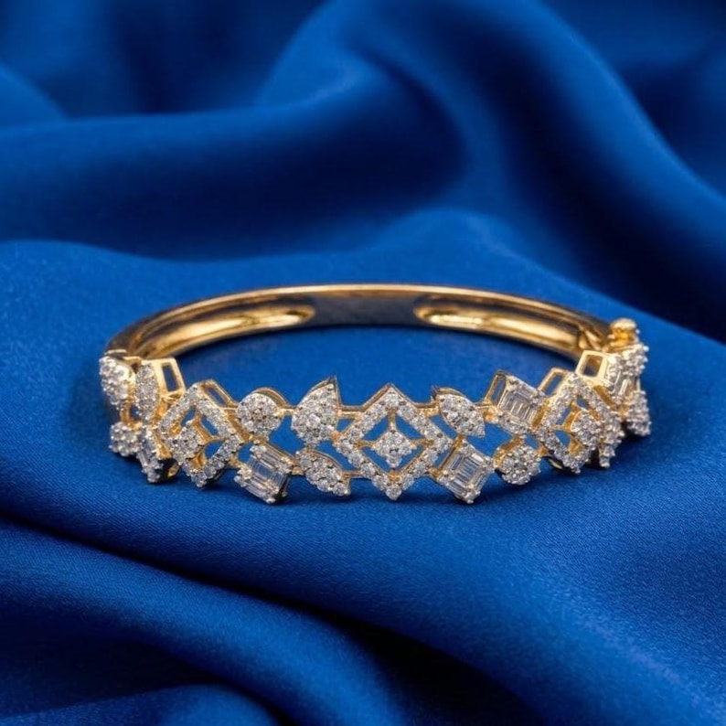 May include: A gold bracelet with a diamond design. The bracelet has a series of geometric shapes and is set against a blue background. The diamonds are clear and sparkle, adding to the bracelet's elegance.