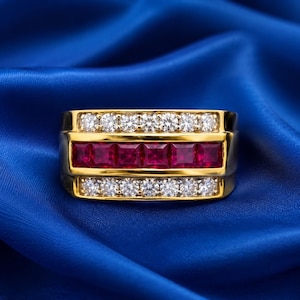 Pode incluir: Um anel de banda de ouro com uma fila central horizontal de cinco rubis vermelhos de corte quadrado, ladeados por duas filas de diamantes brancos de corte redondo. O anel tem um acabamento em ouro polido e um design largo.