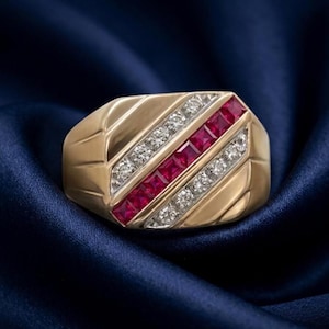 Könnte beinhalten: Ein Goldring mit einem zentralen diagonalen Kanal aus quadratisch geschliffenen roten Rubinen, flankiert von zwei parallelen Kanälen aus rund geschliffenen weißen Diamanten. Der Ring hat eine polierte Oberfläche mit drei Rillen auf jeder Seite.