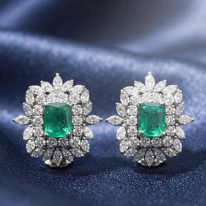 May include: A pair of stud earrings featuring a central emerald-cut green gemstone surrounded by a double halo of small, clear, marquise and round-cut white stones arranged in a floral-inspired pattern with a metallic setting.
