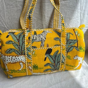 Może przedstawiać: Żółta pikowana torba typu tote z nadrukiem zwierząt safari. Torba ma wzór zebry, lamparta i tukana z zielonymi liśćmi. Torba ma dwa uchwyty i kieszeń z przodu.
