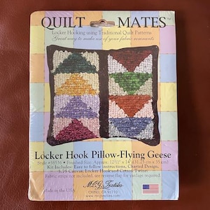 May include: A Quilt Mates locker hook pillow kit with a "Flying Geese" design. The finished size is approximately 12.5" x 14". The kit includes instructions, canvas, hook, and twine. The package has a colorful patchwork background.