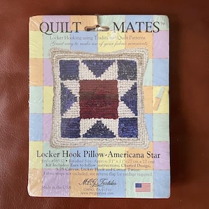 May include: A Quilt Mates kit for a Locker Hook Pillow-Americana Star. The finished size is approximately 11" x 11". The pillow features a star design in shades of blue, red, and cream. The kit includes instructions, canvas, hook, and twine.