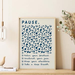 May include: A framed wall art print featuring a cream background with a dark blue floral pattern. The text reads: PAUSE. Relax your forehead. Unclench your jaw. Drop your shoulders. Take a deep breath. Each line is preceded by a small flower icon.