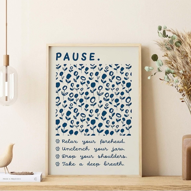 May include: A framed wall art print featuring a cream background with a dark blue floral pattern. The text reads: PAUSE. Relax your forehead. Unclench your jaw. Drop your shoulders. Take a deep breath. Each line is preceded by a small flower icon.