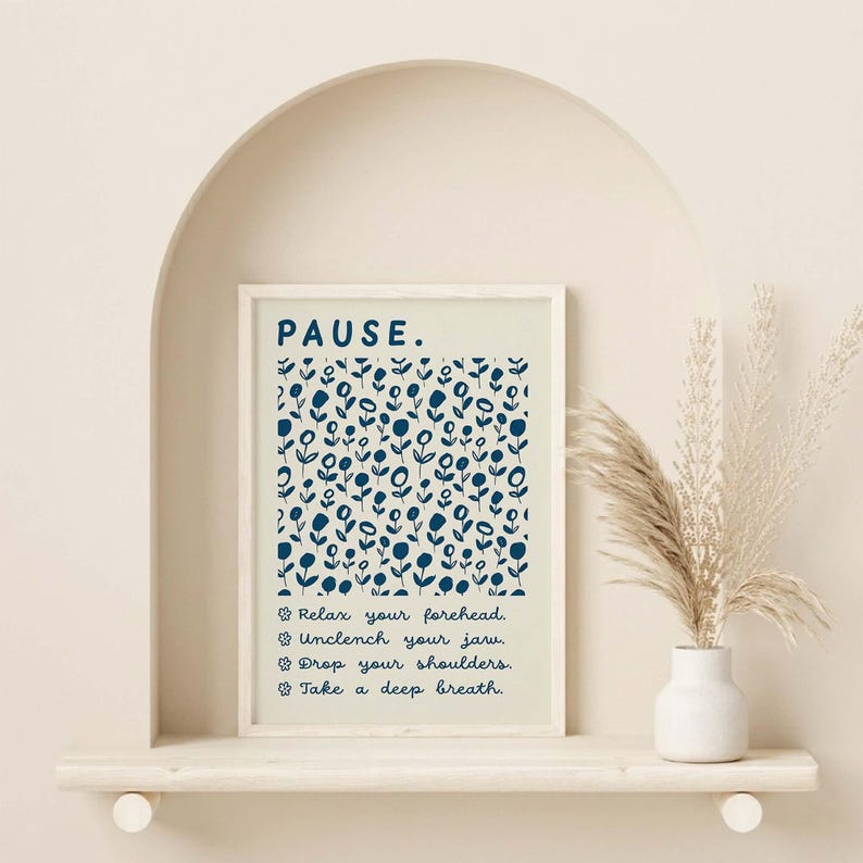 May include: A rectangular wall art print in a light frame featuring the word PAUSE in dark blue, a dark blue floral pattern on a cream background, and four lines of text: Relax your forehead, Unclench your jaw, Drop your shoulders, Take a deep breath.
