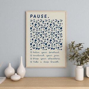 May include: A rectangular wall art print in a light wood frame featuring a cream background with a dark blue floral pattern. The text reads: PAUSE. Relax your forehead. Unclench your jaw. Drop your shoulders. Take a deep breath. Each line is preceded by a small flower icon.