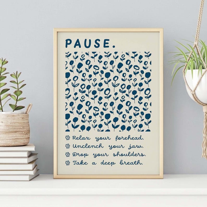 May include: A framed wall art print on a light cream background featuring the word PAUSE in dark blue at the top. Below is a repeating pattern of dark blue stylized flowers. Four lines of text follow, each preceded by a flower icon: Relax your forehead, Unclench your jaw, Drop your shoulders, and Take a deep breath.