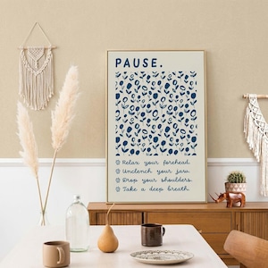 May include: A rectangular wall art print with a cream background featuring the word PAUSE in dark blue, a pattern of small dark blue flowers, and the text: Relax your forehead, Unclench your jaw, Drop your shoulders, Take a deep breath.