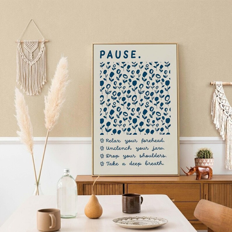 May include: A rectangular wall art print with a cream background featuring the word PAUSE in dark blue, a pattern of small dark blue flowers, and the text: Relax your forehead, Unclench your jaw, Drop your shoulders, Take a deep breath.