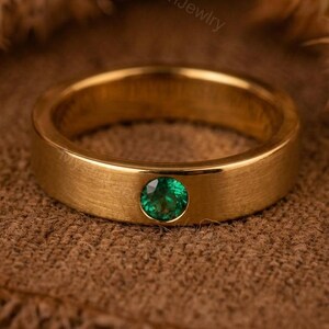 May include: A gold-colored ring with a single, round, emerald-green gemstone. The ring has a brushed metal finish and the text "MysticLabGrownJewlry" is visible in the background.