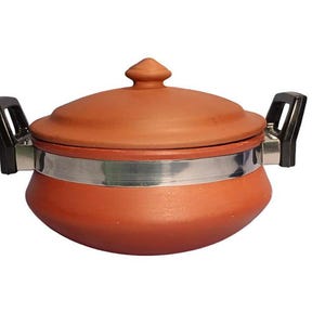 Könnte beinhalten: Ein Kochtopf aus Terrakotta-Ton mit passendem Deckel. Der Topf hat ein silbernes Band in der Mitte und schwarze Griffe auf jeder Seite. Der Deckel hat einen kleinen Knopf oben.