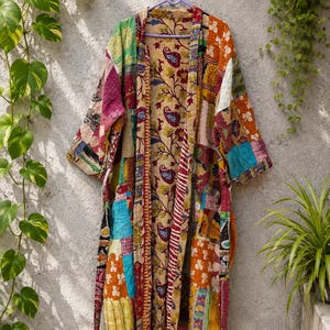 May include: A long-sleeved robe featuring a patchwork design with various colorful fabric squares in shades of red, yellow, blue, and green. The garment has a central panel with a paisley and floral pattern and includes a matching fabric belt.