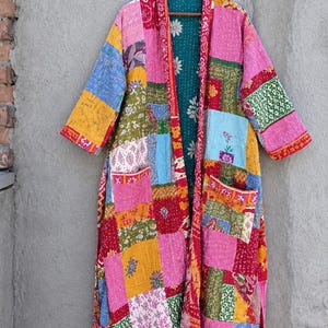 May include: A long-sleeved, open-front robe featuring a patchwork design of various floral and geometric patterns in vibrant shades of pink, yellow, red, blue, and green. The garment includes two front pockets and a contrasting teal interior lining.