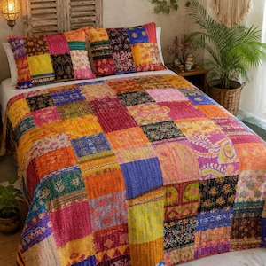 Könnte beinhalten: Eine Patchwork-Tagesdecke und zwei passende Kissenbezüge aus einer lebendigen Anordnung bunter Stoffquadrate. Die Bettwäsche zeigt verschiedene komplexe Muster in Gelb-, Orange-, Rosa-, Blau-, Grün- und Schwarztönen mit sichtbaren Steppnähten.