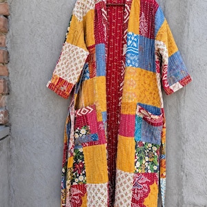 May include: A long-sleeved, knee-length robe featuring a patchwork design of various floral and geometric patterns in shades of red, yellow, blue, and white. The garment has an open front, two front pockets, and a matching tie belt.