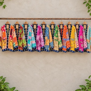 May include: Ten open-front jackets hanging on a wooden rod, each featuring a unique patchwork design with vibrant colors and patterns. Every jacket has a dark blue trim along the collar and front edges, and a numbered tag from one to ten.