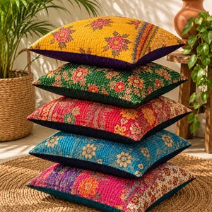 Könnte beinhalten: Ein Stapel aus fünf quadratischen, gesteppten Zierkissen mit lebendigen Blumenmustern in Gelb, Grün, Rot, Blau und Pink. Jedes Kissen hat eine farbenfrohe Oberseite mit feinen Steppnähten und eine einfarbige, dunkle Unterkante.