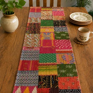 Könnte beinhalten: Ein rechteckiger Tischläufer mit einem Patchwork-Design, das aus verschiedenen Stoffquadraten in leuchtenden Farben wie Pink, Grün, Gelb, Orange und Schwarz besteht. Der Läufer zeigt vielfältige Muster wie florale, geometrische und Paisley-Drucke.