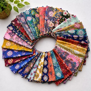 May include: A circular arrangement of multiple folded fabric swatches, each featuring distinct floral patterns in vibrant colours including blue, red, yellow, pink, and green, displayed in a fan-like formation on a plain white surface.