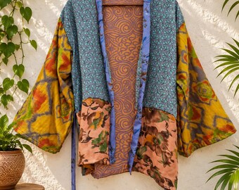 Puede incluir: Una chaqueta estilo kimono de manga larga con un diseño de patchwork que combina varios patrones y colores, incluyendo azul verdoso, amarillo mostaza, naranja y estampados florales. La prenda tiene un borde azul y un cinturón a juego.