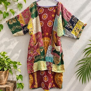 May include: A patchwork kimono jacket featuring a vibrant mix of multicolored fabric squares with intricate kantha stitching. The garment displays a deep red interior lining with circular patterns, wide sleeves, and two front pockets on a hanger.