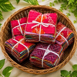 Könnte beinhalten: Eine Sammlung von vier quadratischen Stapeln aus mehrfarbigen Stoffquadraten, die jeweils mit einem weißen Band zusammengebunden sind. Der Stoff zeigt leuchtende Rosa-, Orange- und Violetttöne mit komplexen Mustern und weißen Steppnähten.