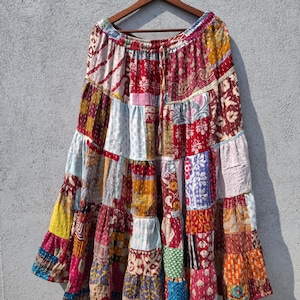 May include: A tiered, ankle-length skirt featuring a patchwork design of various multicolored fabric squares. The skirt has an elasticized waistband with a drawstring and is constructed from multiple layers of stitched, patterned textiles.
