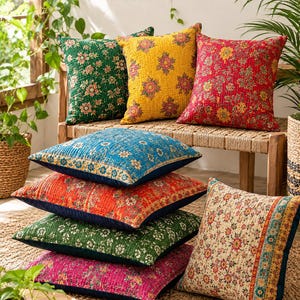 Könnte beinhalten: Eine Sammlung quadratischer Dekokissen mit komplizierten Blumenmustern und gesteppten Texturen. Die Kissen sind in verschiedenen leuchtenden Farben wie Grün, Gelb, Rot, Blau, Orange und Pink gehalten und weisen jeweils detaillierte Steppnähte auf.