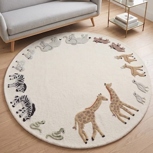 May include: A round, off-white rug featuring an embroidered safari animal design. The rug has a border of various animals, including zebras, giraffes, and elephants. The giraffes are brown with tan spots. The rug is placed on a hardwood floor.