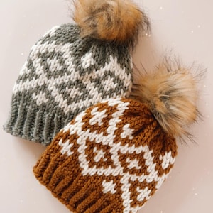 May include: Two knitted winter hats with faux fur pom-poms. One hat is gray with a white geometric pattern, and the other is brown with a white geometric pattern. The hats have a ribbed knit brim.