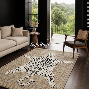 May include: A beige area rug with a leopard print rug on top. The leopard rug has black spots on a cream background. The area rug has a floral border. The room has a sofa, chair, and a view of trees.