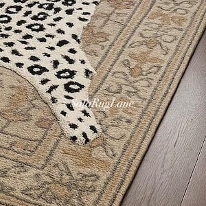 May include: A section of a rug with a leopard print design in cream and black. The rug has a beige border with floral patterns. The rug is on a dark wood floor.