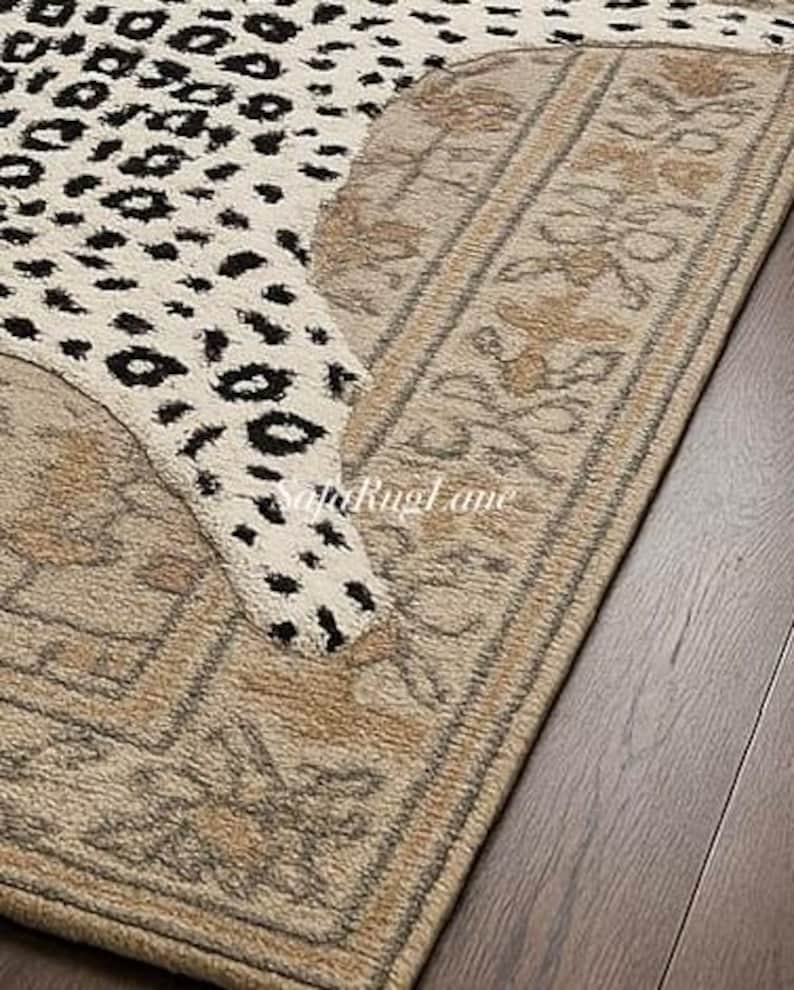 May include: A section of a rug with a leopard print design in cream and black. The rug has a beige border with floral patterns. The rug is on a dark wood floor.
