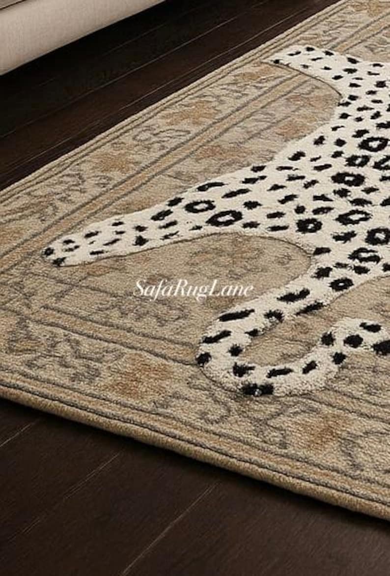 May include: A beige area rug with a leopard pattern in black and white. The rug has a detailed border and is placed on a dark wood floor. The SafaRugLane logo is visible on the rug.
