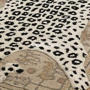 May include: A cream-colored rug with a black leopard print pattern. The rug is shaped like an animal hide and is placed on top of a patterned beige rug.
