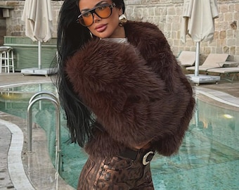 May include: A dark brown faux fur jacket paired with high-waisted brown and black leopard print trousers. The outfit includes a black belt with a silver buckle and oversized amber-tinted sunglasses with thick black frames, worn with gold earrings.