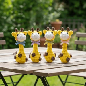 May include: Four handmade crochet giraffe toys. Each giraffe has a yellow body with brown spots, a white face, and a small bow. The giraffes are displayed on a wooden table, with a blurred green background.