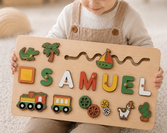 May include: A rectangular wooden name puzzle featuring the name SAMUEL in large, colorful, raised letters. The board includes various wooden shapes such as a green crocodile, palm tree, sailboat, train, gears, llama, and cactus, all with small knobs.