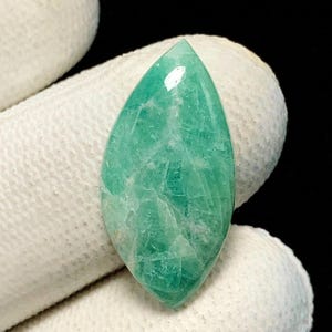 May include: A marquise-cut gemstone with a polished surface, displaying a vibrant sea-green colour with intricate internal veining and natural inclusions. The stone features a pointed top and bottom, showcasing a smooth, reflective finish throughout.