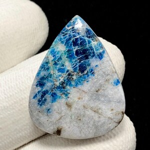 May include: A teardrop-shaped gemstone featuring a polished surface with a mix of vibrant blue and translucent white mineral inclusions. The stone displays a natural crystalline texture with dark veining and a smooth, rounded edge profile.