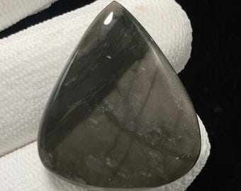 May include: A polished, teardrop-shaped gemstone with a dark, smoky gray color and a glossy finish. The stone has a smooth surface with subtle light and dark variations, and is held by a gloved hand.
