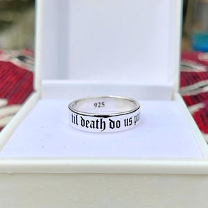 Puede incluir: Un anillo de plata con la inscripción "til death do us part" en letras negras. El anillo está dentro de una caja blanca. El anillo está marcado con "925".