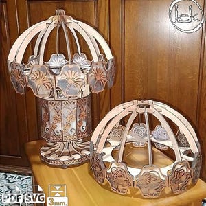 Könnte beinhalten: Zwei dekorative Holzstrukturen im Karussell-Stil. Eine ist hoch und zylindrisch, die andere eine kürzere, offene Schalenform. Beide weisen aufwendige Blumenausschnitte und eine helle Holzoberfläche auf. Die Strukturen stehen auf einer Holzoberfläche.