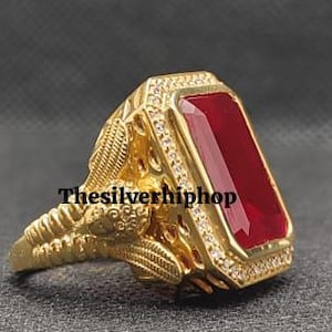 Könnte beinhalten: Ein goldfarbener Ring mit einem großen, rechteckigen, tiefroten Edelstein. Der Ring hat aufwendige Details um den Edelstein und am Band. Der Text "thesilverhiphop" ist sichtbar.