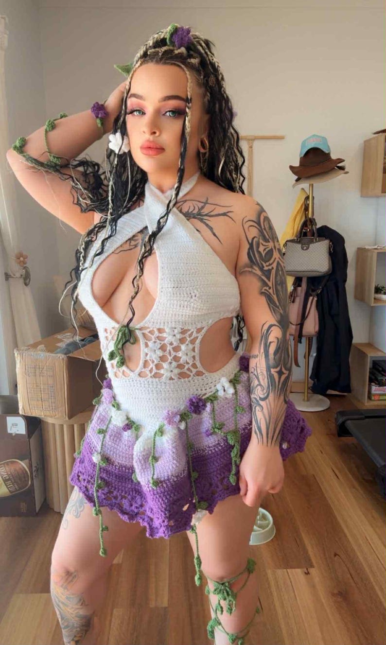 May include: A white halter top and a purple crochet skirt with floral and vine accents. The outfit is handmade and features a unique design. The model is wearing accessories that match the outfit.